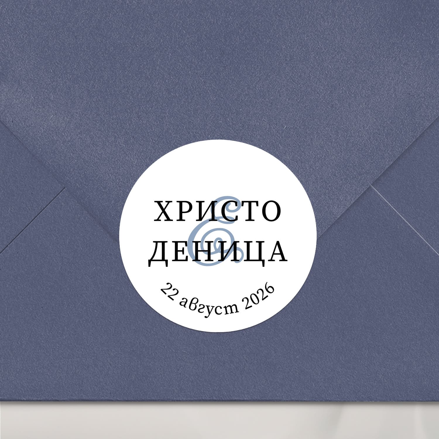 Персонализиран стикер с изчистен шрифт и син амперсанд, залепен върху тъмносин плик – стилен етикет за сватбена покана или подарък.