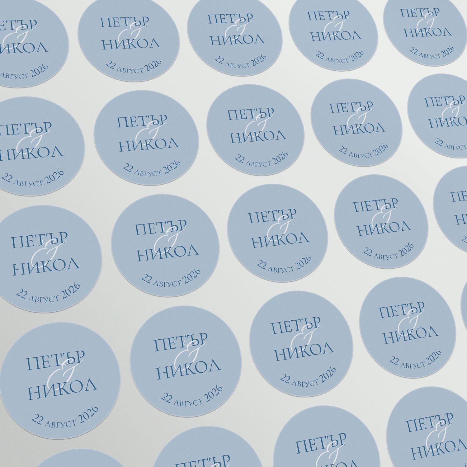 Персонализирани кръгли стикери със светлосин фон и тъмносин текст, подредени върху лист – елегантен детайл за сватбени сувенири.