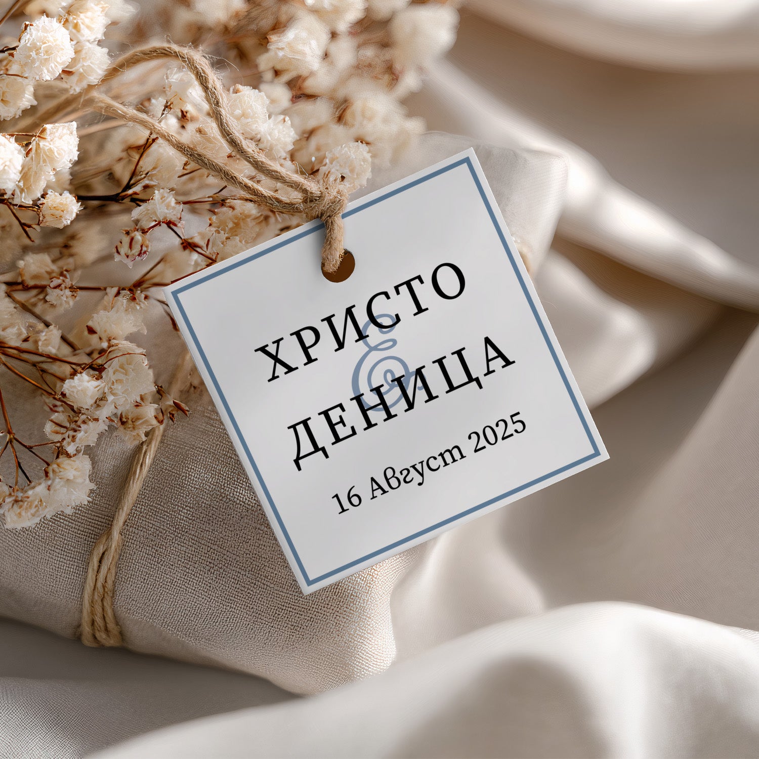 Персонализиран сватбен таг с нежен син кант и черен надпис, завързан с канап – подходящ за естествен декор и лятна сватба.